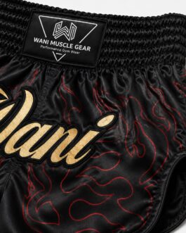 Close-up of gold Wani logo and red flame sublimation print on black satin boxing shorts