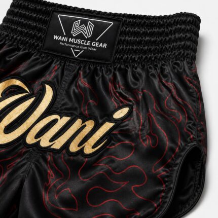 Close-up of gold Wani logo and red flame sublimation print on black satin boxing shorts