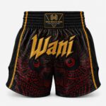 : Black and red satin Muay Thai boxing shorts with gold Wani logo, front view