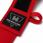 Close-up of red Wani Muscle Gear hand wrap showing woven brand label, hook-and-loop closure, and thumb loop stitching