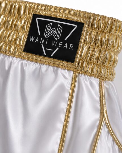 Home Close-up of white and gold satin boxing shorts waistband with Wani Wear logo patch
